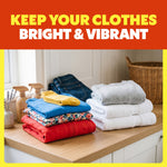 Folded colorful and white clothing stacks on a wooden counter in a bright laundry room beneath a keep clothes bright message