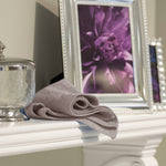 Folded light-gray microfiber cloth styled on a white mantel next to a silver jar and framed purple floral photo