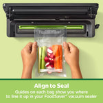Hands holding a FoodSaver vacuum bag of vegetables being aligned into a vacuum sealer machine
