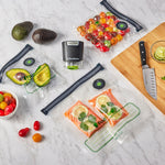 FoodSaver vacuum zipper bags filled with produce and salmon arranged with handheld sealer and cutting board