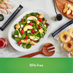 Styled overhead scene with a salad plate and FoodSaver reusable zipper bags holding sliced fruit and a handheld vacuum sealer nearby