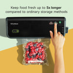 Hand pressing button on a black FoodSaver vacuum sealer with a sealed bag of red berries hanging below