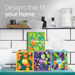 Bathroom shelf display of four colorful Kleenex decorative cube boxes with one box elevated and a tissue pulled from the top.