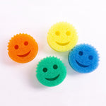 Four round smiling Scrub Daddy sponges in orange, yellow, green and blue arranged on a white background