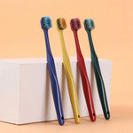 Four upright manual toothbrushes in blue, yellow, red and green with angled heads, displayed against a peach background.