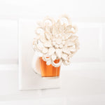 Fragrance oil refill inserted in a decorative plug-in warmer with a floral ornamental cover on a tiled wall