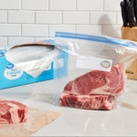 Clear gallon freezer bag with raw steak inside sits on a countertop next to an open Great Value box of bags.