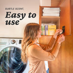 Woman attaching a Fresh Wave pod to the inside of a cabinet door with laundry machine and Fresh Wave packets on a shelf nearby