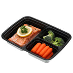 Black three-compartment meal prep container filled with salmon, broccoli and baby carrots on a white background