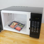 Meal prep container with clear lid inside a microwave, containing salmon, broccoli and carrots on a glass turntable