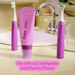 Bathroom countertop scene showing two fuchsia electric toothbrushes flanking a matching tube of Frida fluoride toothpaste.