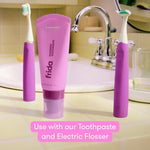 Bathroom scene with two purple Frida electric toothbrushes flanking a tube of Frida fluoride toothpaste on a tile sink