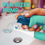 Hand dispensing a pea-sized pump of Frida toothpaste onto a toothbrush over a sink