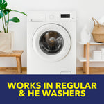Front-loading washing machine in a styled laundry room setting above a banner reading 'Works in Regular & HE Washers'