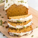 Sliced frosted loaf topped with pumpkin seeds on a wooden cutting board, three slices fanned in front.