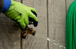 G & F glove in use turning an outdoor faucet, showing green back and navy foam palm gripping a valve