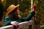 Gardener wearing a straw hat with G & F grey knit gloves, one glove with pink-coated palm visible on a fence.