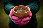 Person holding a terracotta pot wearing G & F grey knit gloves with bright pink rubber-coated palms.