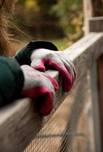 Close-up of G & F grey knit gloves with pink rubber-coated fingertips resting on a wooden railing.
