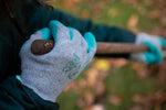 Hands wearing G & F grey knit gloves with teal rubber-coated palms gripping a wooden handle outdoors.