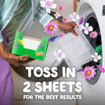 Hand holding a dryer sheet over a washing machine with an open Gain box and overlayed floral graphics