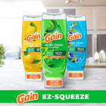 Three upright Gain Ultra Clean EZ‑Squeeze bottles in different scent colors on a kitchen counter with 'no flip no mess' caps