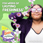 Person enjoying scent with oversized Gain fabric softener bottle and flowers, headline promises weeks of lasting freshness