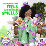 Smiling person holding a green towel surrounded by purple flowers with Gain fabric softener bottle and headline about laundry feeling as good as it smells