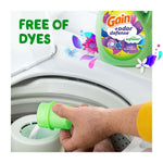 Hand pouring liquid from a green measuring cap into a washing machine dispenser with a Gain bottle inset and 'free of dyes' text