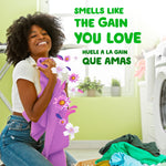 Happy person hugging a purple towel in a laundry room with floral scent graphics and headline about smelling the Gain you love