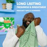 Smiling man holding a striped shirt near a Gain powder lavender box and headline about long lasting freshness