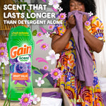 Person smelling a purple garment next to a Gain Moonlight Breeze scent booster bottle and decorative floral graphics