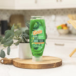 Lifestyle photo of a green Gain Ultra Clean bottle on a wooden board in a kitchen setting with plant and blurred background