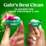 Two laundry pacs held between fingers comparing larger pink-and-green Gain plus pod to smaller classic pod on green background