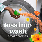 Hand tipping a green measuring cup pouring orange scent-beads into a front-load washer with floral accents and ‘toss into wash’ text