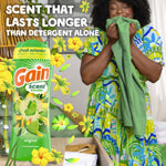 Woman smelling laundry next to a large Gain scent booster bottle and floating yellow floral graphics and text.