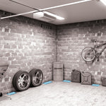 Grayscale garage interior scene with automotive tires, bike and several blue glue trays placed along the floor as pest-control placement examples