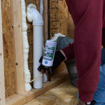 Photo of a person applying GE Pest Block insulating foam around a PVC pipe in a framed wall cavity.