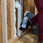 Close view of someone dispensing GE Pest Block foam around a plumbing pipe inside an unfinished wall.