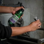 Person spraying Gear Hugger Eco degreaser on a metal part held over a workshop machine, visible stream of spray.
