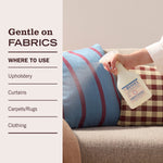 Demonstration image of a hand spraying Mrs. Meyer’s fabric freshener onto a sofa cushion with usage suggestions at left.