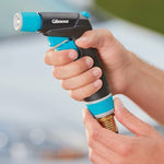 Gilmour front trigger nozzle held in two hands, showing brass hose connector, teal accents and logo