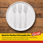Three clear plastic forks arranged on a white plate over a wooden table with Glad branding panel