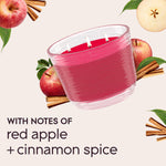 Angled pink three-wick Glade candle with apples and cinnamon graphics and text noting red apple and cinnamon spice notes