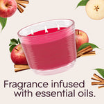 Pink three-wick Glade candle with burning wicks surrounded by apples and cinnamon sticks with text about essential oils