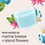 Tilted aqua-blue three-wick candle illustration surrounded by tropical flowers and text noting 'with notes of marine breeze + island flowers'