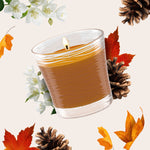 Close-up lit Glade Cashmere Woods candle surrounded by pinecones, blossoms and autumn leaves on a neutral background