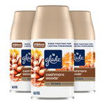 Three Glade Cashmere Woods automatic spray refill cans with pinecone artwork on a white background