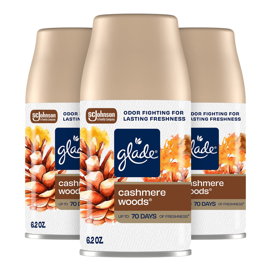 Three Glade Cashmere Woods automatic spray refill cans with pinecone artwork on a white background