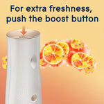 Close-up of dispenser top with an arrow pointing to the boost button and citrus artwork in the background